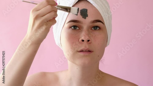 Young woman apply clay facial mask. Face peeling mask with charcoal, spa beauty treatment, skincare, cosmetology. Close up