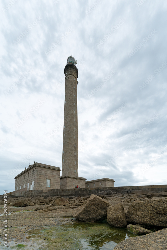 tall stone lighthouse with rocky shore at low tide under a stormy sky