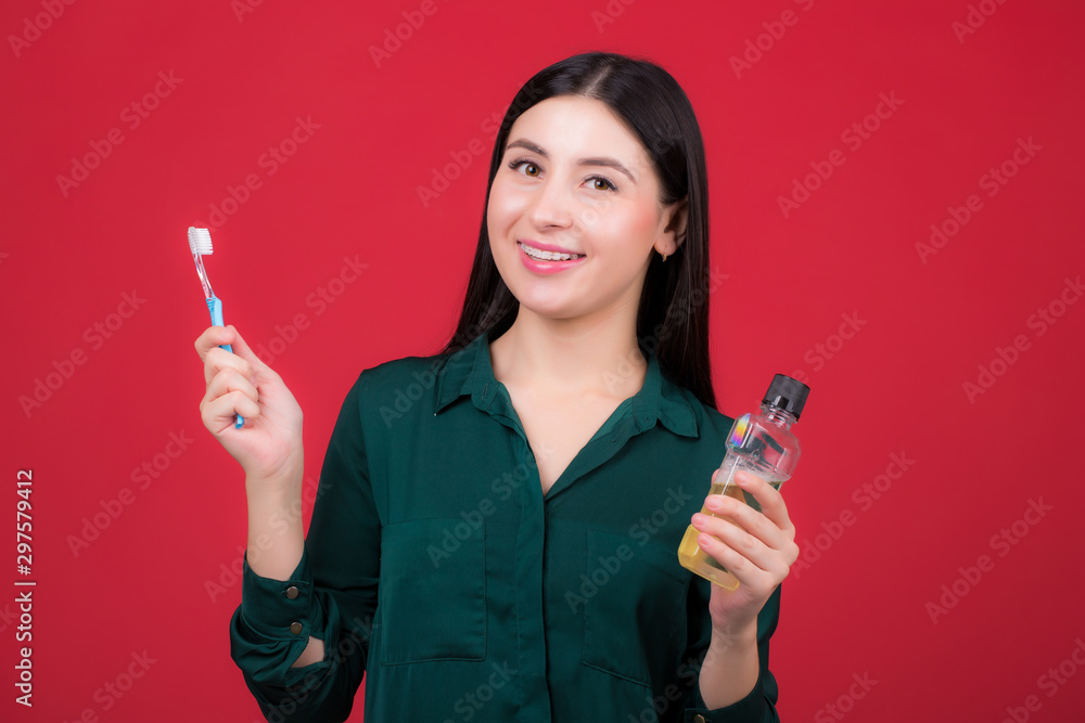 Young smiling woman with a toothbrush in hand, posing in studio on a red background Young smiling woman with a toothbrush in hand, posing in studio on a red background
