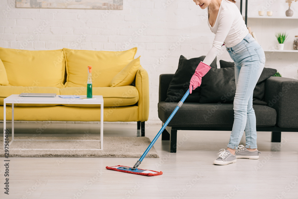 cropped view of housewife washing floor with mop near yellow and grey sofas cropped view of housewife washing floor with mop near yellow and grey sofas