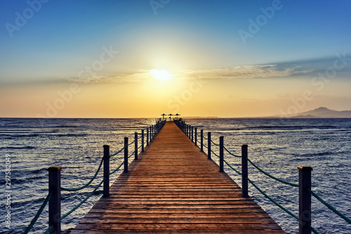 Bright and colorful sunrise over the sea and pier. Perspective view of a wooden pier on the sea at sunrise with rocky islands in the distance