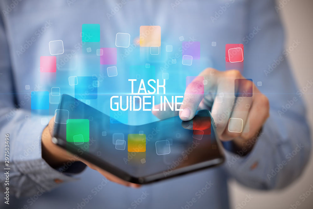 Young man holding a foldable smartphone with TASK GUIDELINE inscription, educational concept Young man holding a foldable smartphone with TASK GUIDELINE inscription, educational concept