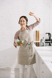 happy young woman in headphones dancing and singing while holding bowl with salad