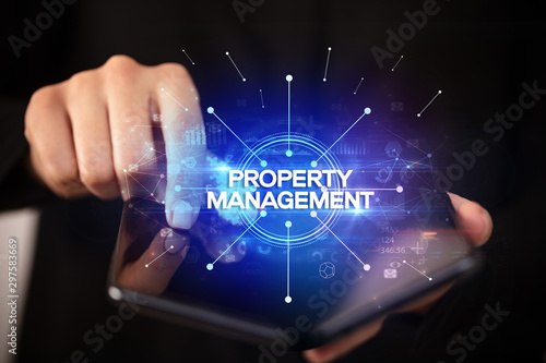 Businessman holding a foldable smartphone with PROPERTY MANAGEMENT inscription, new business concept