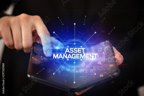 Businessman holding a foldable smartphone with ASSET MANAGEMENT inscription, new business concept