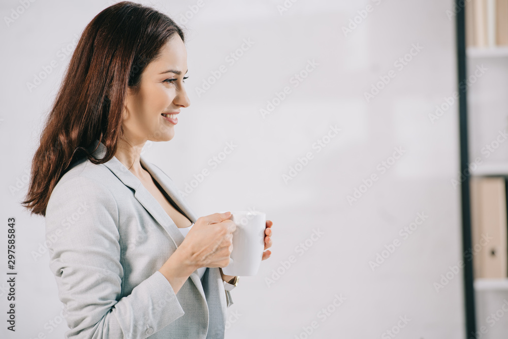 smiling, young secretary looking away while holding coffee cup smiling, young secretary looking away while holding coffee cup