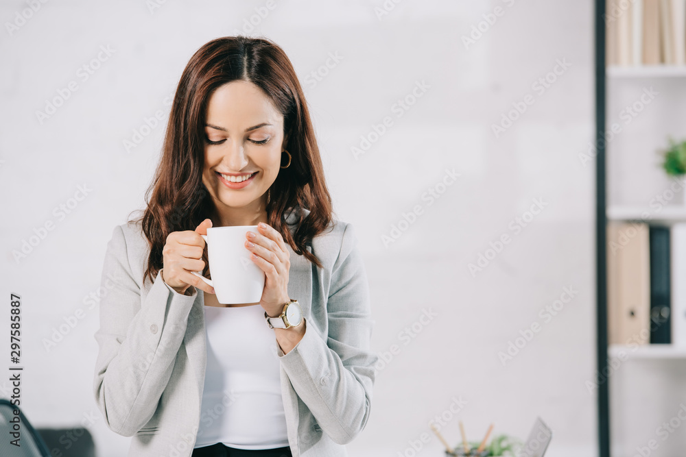 attractive, young secretary smiling while holding coffee cup in office attractive, young secretary smiling while holding coffee cup in office