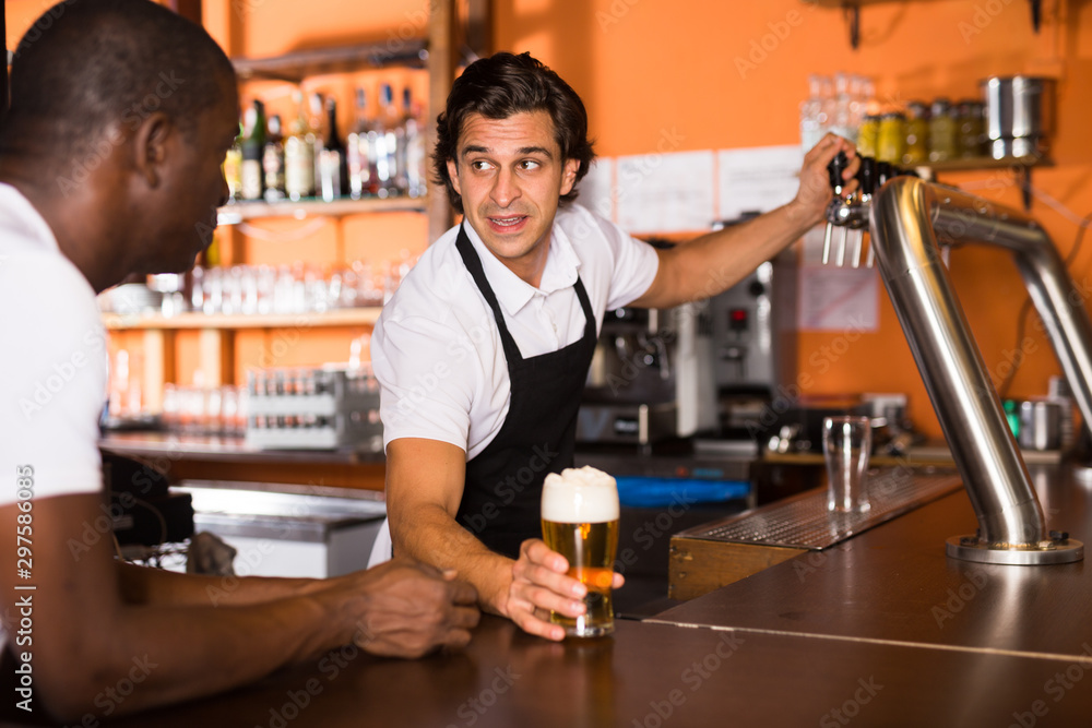 Smiling man barman giving glass of golden beer to client