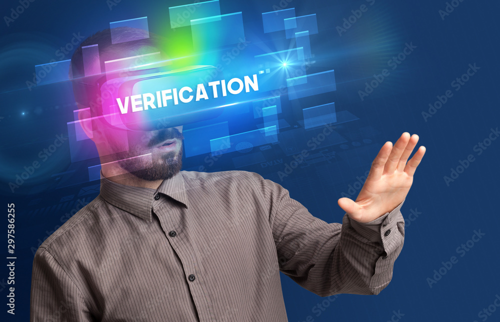 Businessman looking through Virtual Reality glasses with VERIFICATION inscription, innovative security concept Businessman looking through Virtual Reality glasses with VERIFICATION inscription, innovative security concept