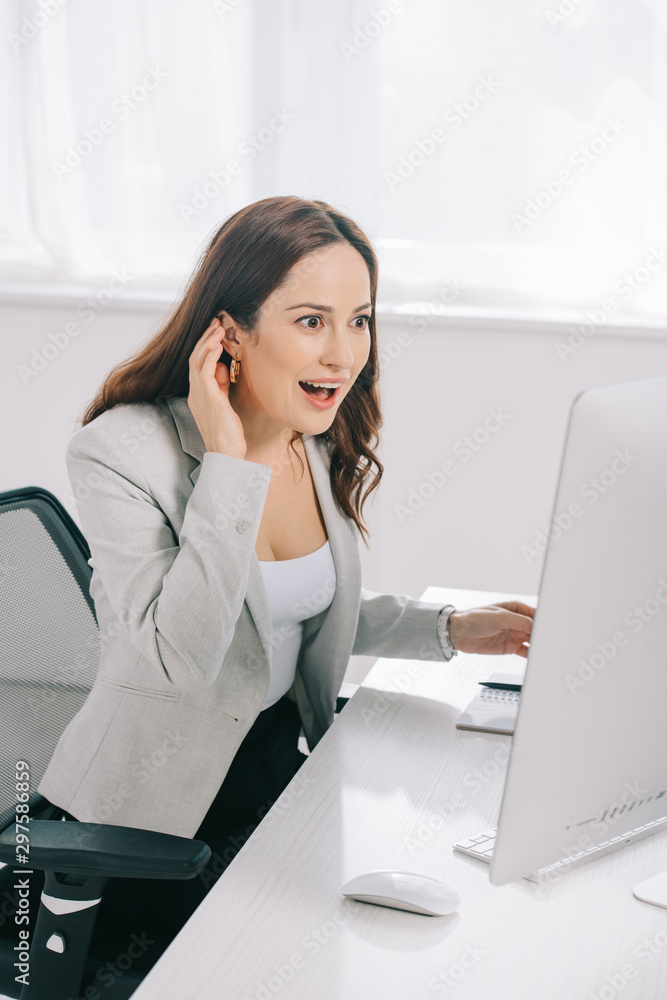 excited, surprised secretary looking at computer monitor while sitting at workplace excited, surprised secretary looking at computer monitor while sitting at workplace
