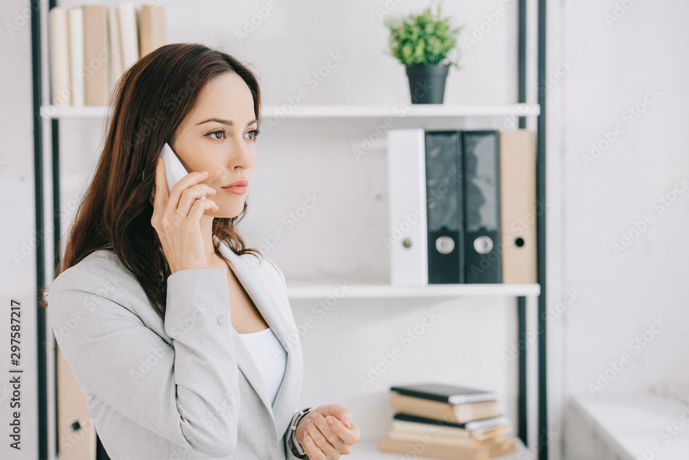 attractive, thoughtful secretary looking away while talking on smartphone in office attractive, thoughtful secretary looking away while talking on smartphone in office
