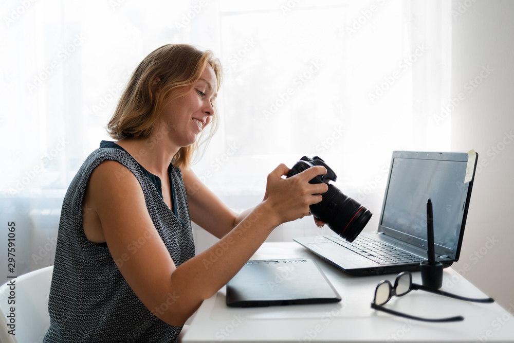 Business and creativity. A young woman smiling and looks at the pictures on the camera. Nearby lies a tablet and a laptop with glasses Business and creativity. A young woman smiling and looks at the pictures on the camera. Nearby lies a tablet and a laptop with glasses