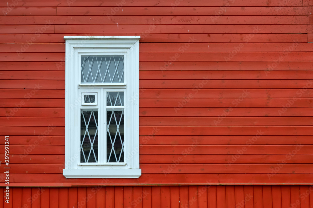 Fragment of a wall of a wooden house with a window. The wall is made in the old style of boards and painted in red. The window has a white frame and platband. Background. Texture. Fragment of a wall of a wooden house with a window. The wall is made in the old style of boards and painted in red. The window has a white frame and platband. Background. Texture.