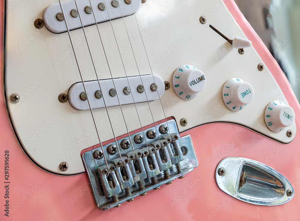 close up of an old style pink electric guitar. Details of rock guitar.  Strings and volume control. Part of modern electric six string guitar pink  color with glossy finish. Stock Photo