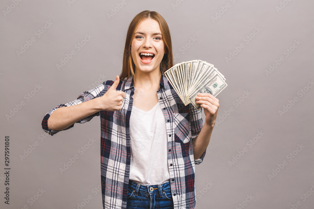 Portrait of a playful young woman with long hair holding bunch of money banknotes and looking at camera, copy space, isolated over grey background. Thumbs up. Portrait of a playful young woman with long hair holding bunch of money banknotes and looking at camera, copy space, isolated over grey background. Thumbs up.