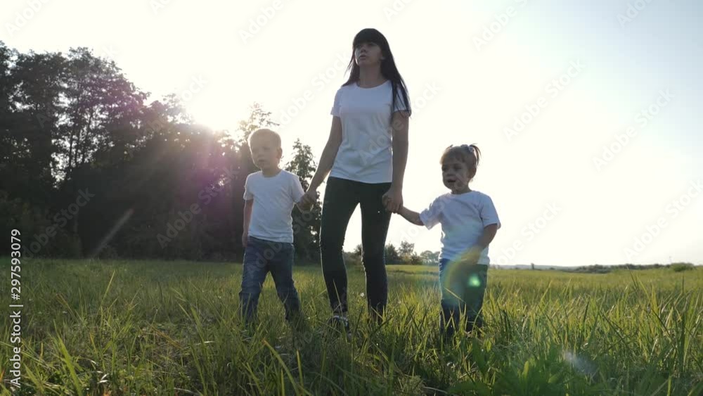 A young mother walks with her children on the green grass. Happy family having fun spending their day off in the fresh air. A young mother walks with her children on the green grass. Happy family having fun spending their day off in the fresh air.