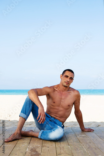 young muscular man in denim pants resting and posing on the beach