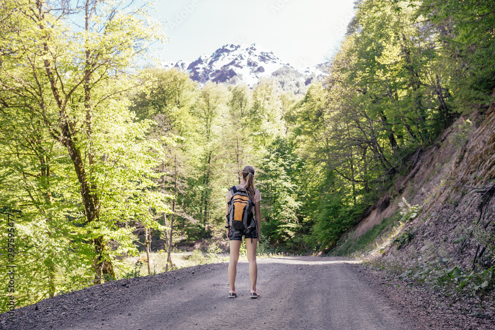 Rear view of a slim young brave girl traveling in the mountains alone on a summer sunny day. The concept of the spirit of competition and new discoveries