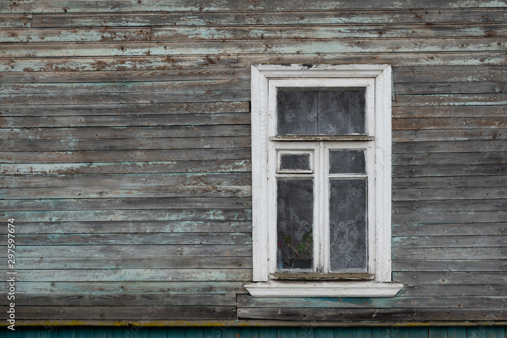 Wall of an old wooden house. The paint on the boards almost disappeared, the wooden parts look aged. There is a window with a white platband. Background. Texture.