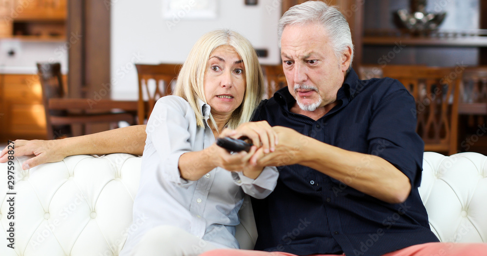 Mature couple fighting for remote control on a sofa Mature couple fighting for remote control on a sofa