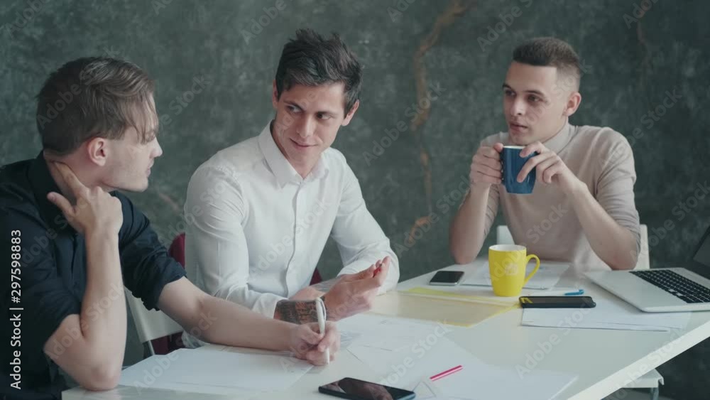 three men discuss a project and plan while sitting at a table in an office three men discuss a project and plan while sitting at a table in an office