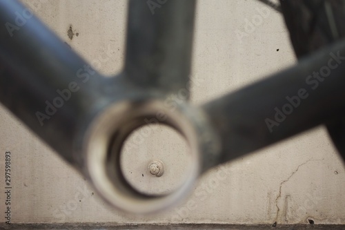 Looking through the unfocused bottom bracket shell of a biciycle frame at the concrete wall behind with a little snail climbing on it photo