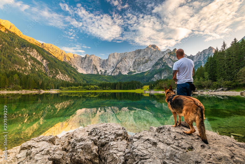 Tattoed Man with Dog Looking at Beautiful Lake and Mountains. Outdoor Active  Lifestyle - obrazy, fototapety, plakaty 
