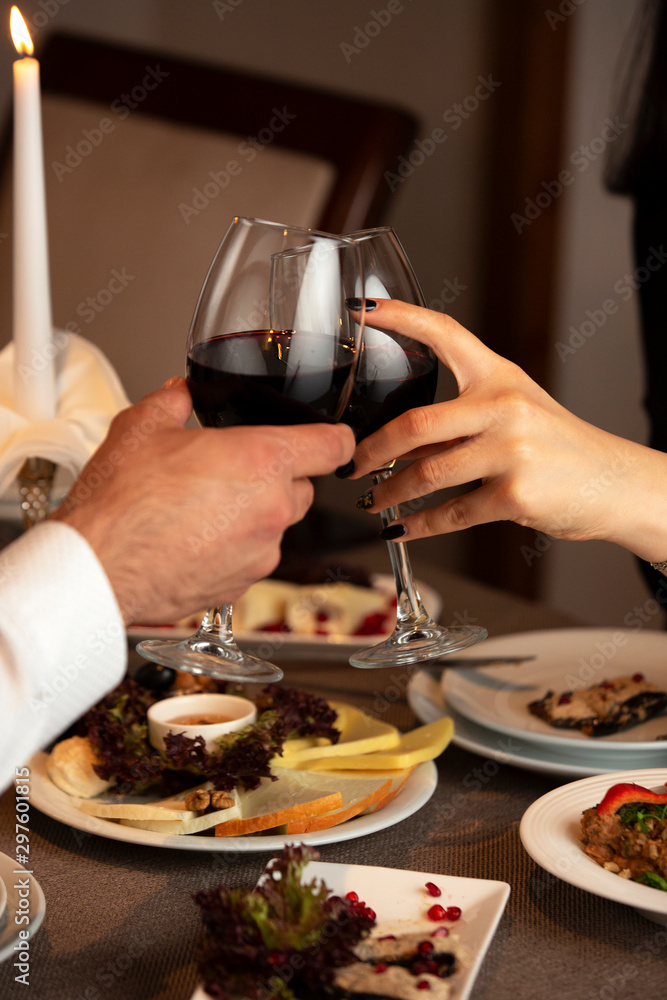 close up of couple hands cheering red wine glasses at dinner