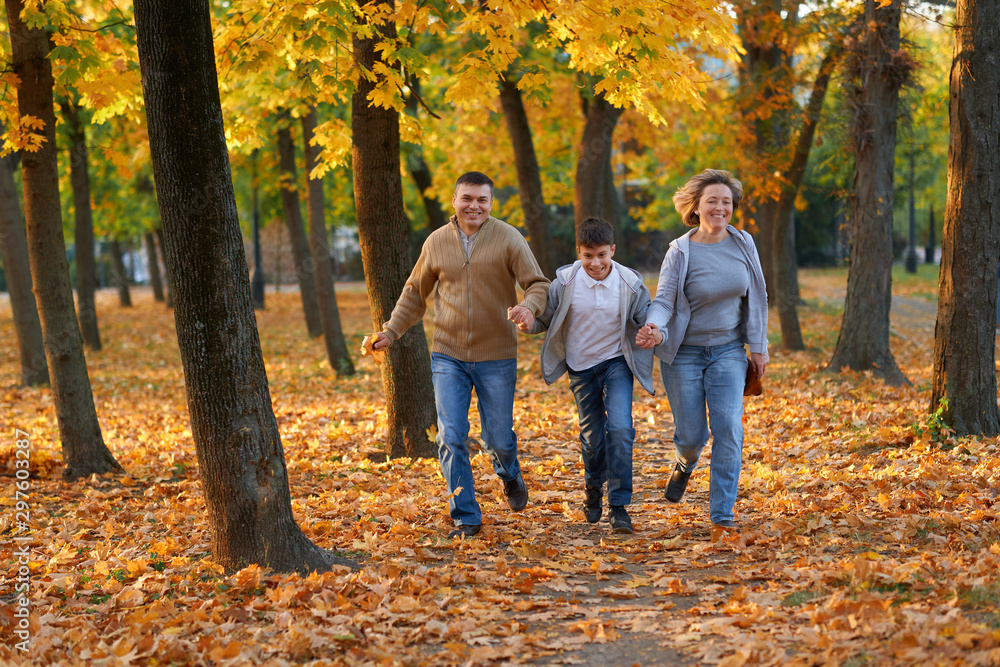 Obraz premium Happy family having holiday in autumn city park. Children and parents running, smiling, playing and having fun. Bright yellow trees and leaves