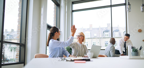 Two smiling businesswomen celebrating with high fives in an offi