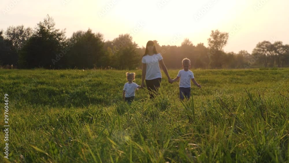 A young mother walks with her children on the green grass. Happy family having fun spending their day off in the fresh air. A young mother walks with her children on the green grass. Happy family having fun spending their day off in the fresh air.