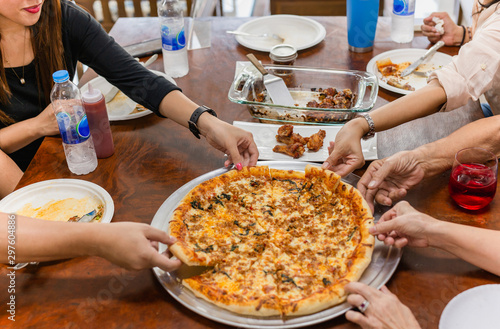 Top view family members having lunch hands reaching out for slice pizza on table.
