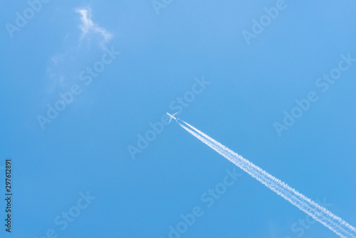 Airplane in a blue sky with clouds and condensation trails, Germany