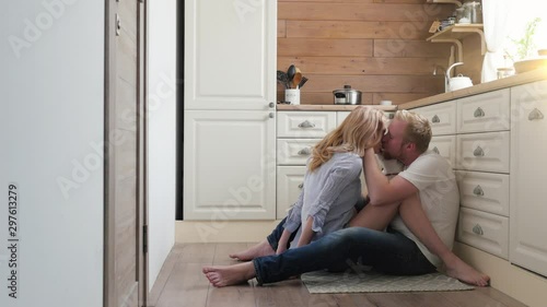 pregnant wife sitting on the floor with her husband. a man and a pregnant woman are sitting at the back of their kitchen and kissing. Scandinavian style. photo