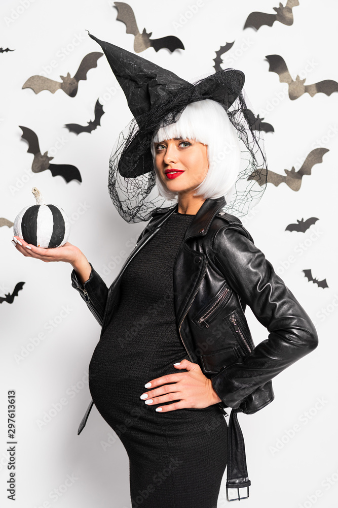 pregnant woman in witch hat and wig holding pumpkin in Halloween pregnant woman in witch hat and wig holding pumpkin in Halloween