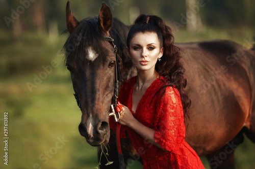 Girl in a long dress stands near a horse, a beautiful woman strokes a horse and holds the bridle in a field in autumn. Country life and fashion, noble steed