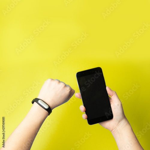 Female hands hold a smartphone and a fitness bracelet on hand. photo