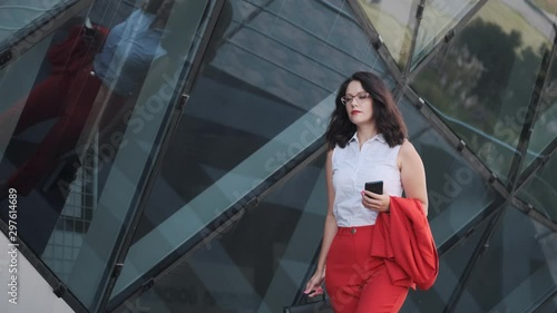 Confident business woman in a strict red suit uses a smartphone on the go