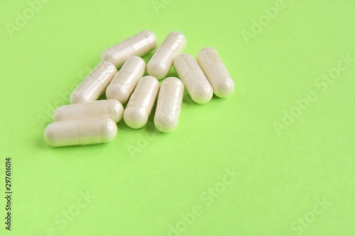 Pile of white capsules for health care with selective focus on neon green background. Pharmacology supplements on neon green backdrop with empty space for text. Medicine pills. Vitamins