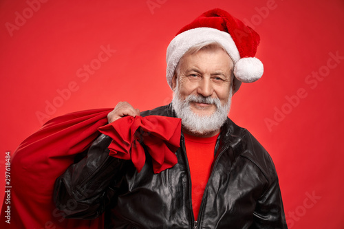 Elder grey-haired man in Santa hat with red sack in studio