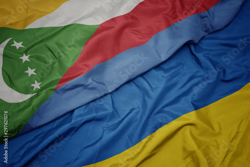 waving colorful flag of ukraine and national flag of comoros.