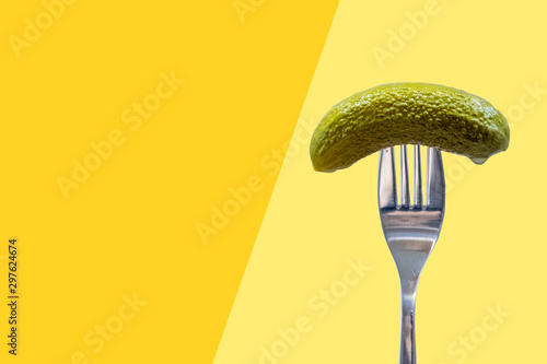 Fotografie Pickle on fork, dill, gherkin, yellow and orange background, national pickle day