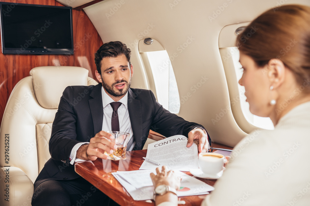 businessman with glass showing contract to businesswoman in private plane businessman with glass showing contract to businesswoman in private plane