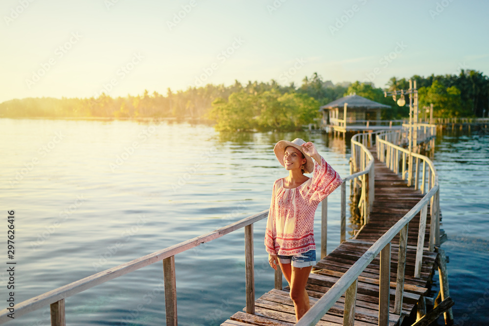 Vacation on tropical island. Young woman in hat enjoying sunset sea view from wooden bridge terrace, Siargao Philippines.