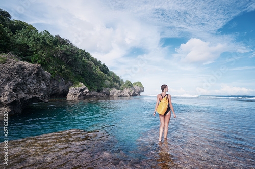 Tropical traveling. Young woman with waterproof backpack walking by low tide sea beach.