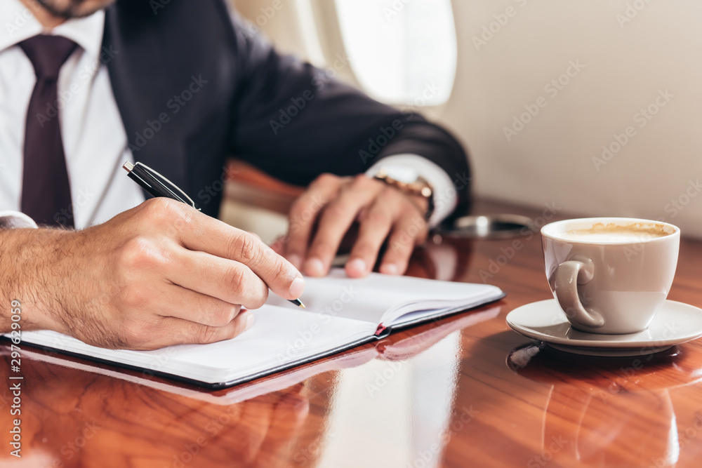 cropped view of businessman writing in notebook in private plane cropped view of businessman writing in notebook in private plane