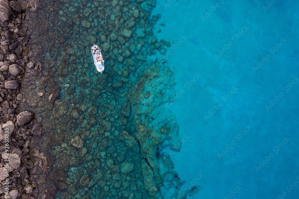 Fototapeta premium An aerial view of a boat the beautiful Mediterranean sea, where you can se the rocky textured underwater corals and the clean turquoise water of blue lagoon Agia Napa