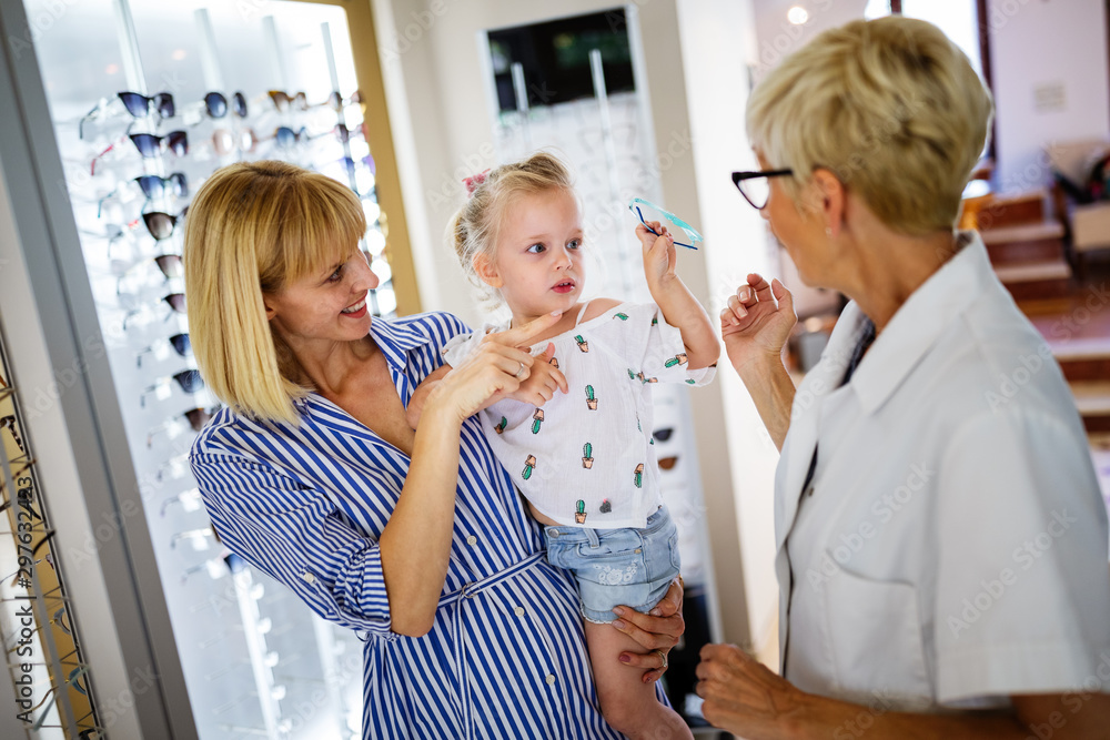 Optician helping to find a perfect glasses to little girl at optics store Optician helping to find a perfect glasses to little girl at optics store