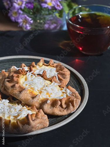 Karelian Pirakka pies located on a gray plate on a black stone background. Near a cup of tea. Traditional dish of Karelia and Finland from rye flour with different fillings. Close-up