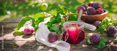 Glass jar with plum jam confiture and ripe plum berries in a basket on a wooden vintage table in the garden with a copy space, the idea of home canning and organic ecological bio nutrition